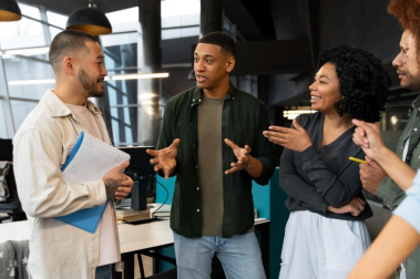 A cena mostra uma equipe em interação no ambiente de trabalho, reforçando que comunicação, escuta ativa e colaboração são competências essenciais no desenvolvimento de software.